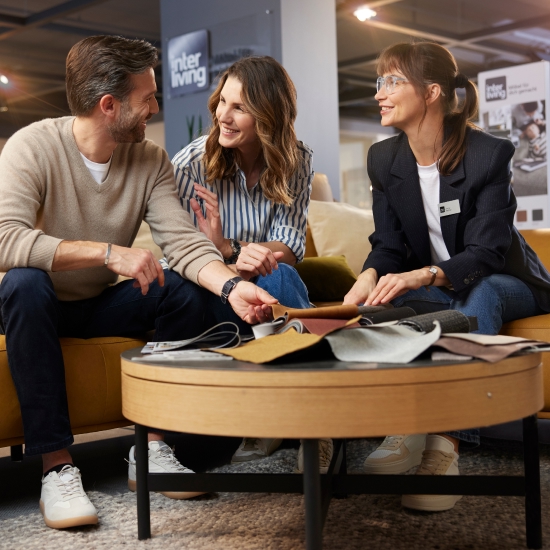 Ein Pärchen lässt sich bei Weser Wohnwelt individuell zu Interliving Möbeln beraten. Drei Personen sitzen in einem gemütlichen Raum und besprechen die besten Einrichtungsmöglichkeiten.
