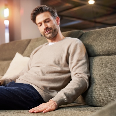 Ein Mann sitzt im Eirichtungshaus Weser Wohnwelt und betrachtet fasziniert ein hochwertiges Interliving Sofa, beeindruckt von Design und Qualität.